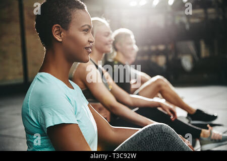 Fit young African American woman sitting on the floor of a gym with other people before a workout class Stock Photo