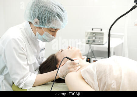 Medical treatment removal of birthmark from female patient's neck. Female dermatologist surgeon using a professional electrocautery for removing mole. Stock Photo