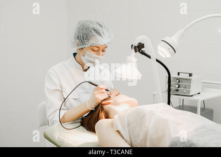 Medical treatment removal of birthmark from female patient's face. Female dermatologist surgeon using a professional electrocautery for removing mole. Stock Photo