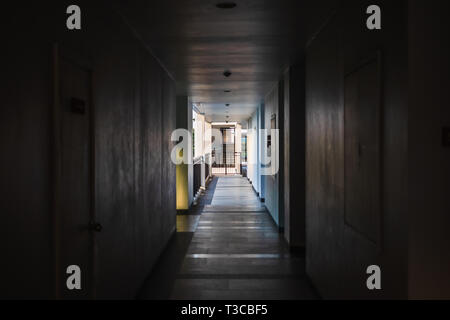 Perspective of empty corridor in apartment building with doors and and fire escape and light in the end of the way. Stock Photo