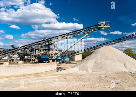 Conveyor over heaps of gravel on blue sky at an industrial cement plant. Stock Photo