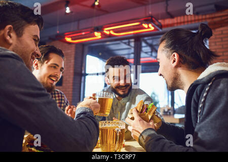 Happy friends eat burgers, drink beer in a bar. Stock Photo
