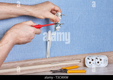 Electrician is tiwisting screw in new electric outlet with screwdriver. Stock Photo