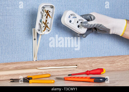 Worker in protective gloves is installing wall plug socket, there are hand tools on the floor. Stock Photo
