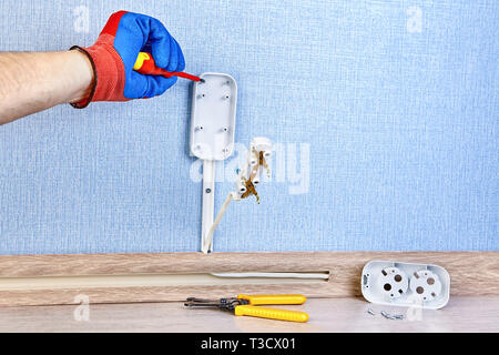 Electrician in protective gloves is twisting screw in new wall socket, residential wiring work. Stock Photo