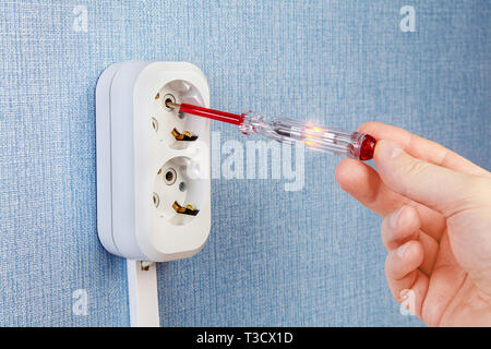 Checking the voltage in the outlet using electrical tester screwdriver or voltage detector, close-up. Stock Photo