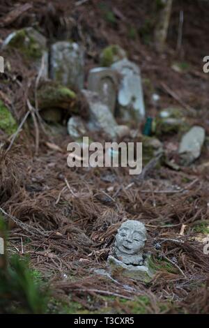 A fallen Jizo statue head on the ground next to crumbling old grave stones at Okunoin cemetery in Koyasan, Japan. Stock Photo