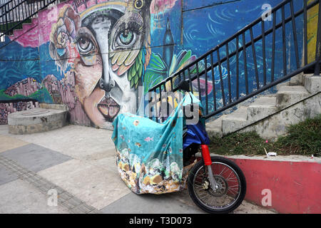 Motorcycle under Colorful Cover in Front of Vibrant Mural in Comuna 13, Medellin, Colombia Stock Photo