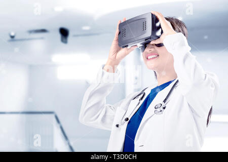 Asian female doctor in white coat and stethoscope using virtual reality device on the hospital. Augmented reality technology Stock Photo