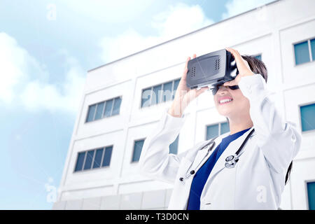 Asian female doctor in white coat and stethoscope using virtual reality device with hospital background. Augmented reality technology Stock Photo