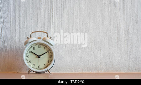 White vintage alarm clock displaying 10:10 am or pm on wooden table and white wall background. Stock Photo