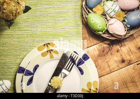 Easter table setting with colorful eggs and spring flowers on wooden table, top view. Vintage toned photo. Stock Photo