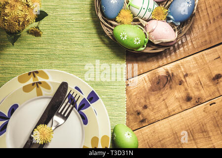Easter table setting with colorful eggs and spring flowers on wooden table, top view. Vintage toned photo. Stock Photo