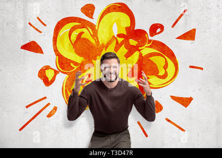 Young man in casual clothes making brain explosion gesture with cartoon explosion drawn on white wall background. Stock Photo