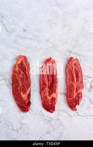 raw marbled beef steaks at white marble background. copy space. vertical Stock Photo