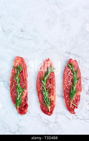 raw marbled beef steaks with green rosemary branch and sea salt at white marble background. Copy space. vertical Stock Photo