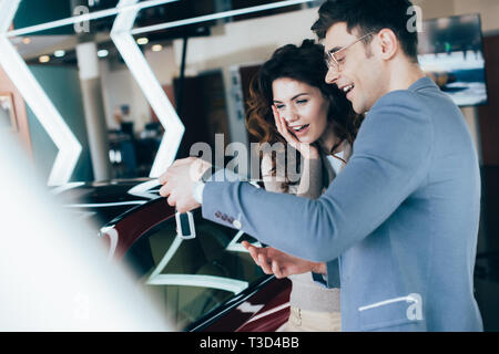 attractive surprised woman standing with handsome man and looking at keys near car Stock Photo