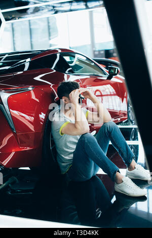 upset man sitting near red automobile in car showroom Stock Photo
