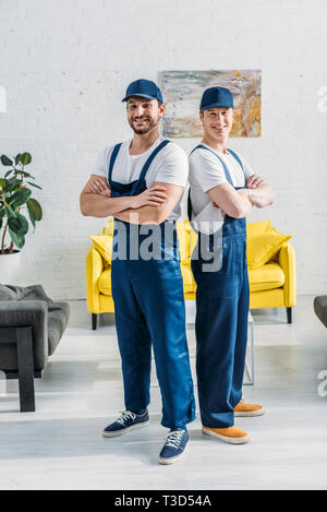 handsome movers with arms crossed looking at camera and smiling in apartment Stock Photo