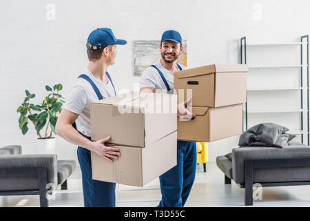 two movers in uniform looking at each other while carrying cardboard boxes in apartment Stock Photo