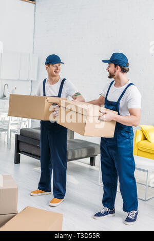 two smiling movers transporting cardboard boxes in apartment Stock Photo