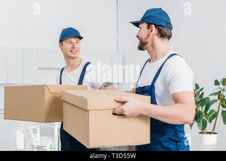two smiling movers transporting cardboard boxes in apartment Stock Photo