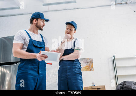 two handsome movers in uniform using digital tablet in apartment with copy space Stock Photo