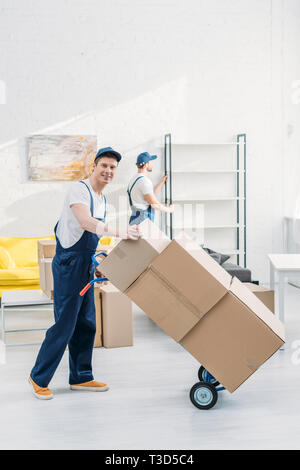 two movers in uniform transporting cardboard boxes and furniture in apartment Stock Photo