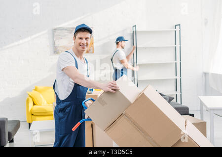 two movers in uniform transporting cardboard boxes and furniture in apartment Stock Photo