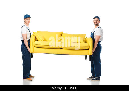 two smiling movers transporting yellow sofa and looking at camera on white Stock Photo