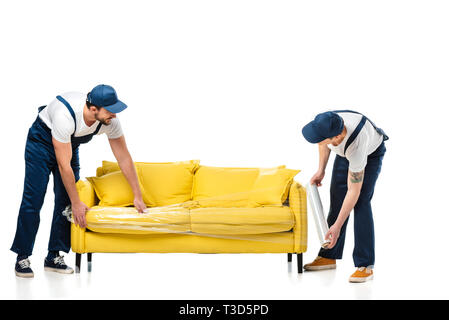 two movers wrapping yellow sofa with roll of stretch film on white Stock Photo