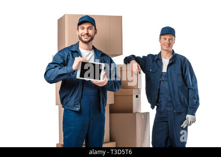 two movers with cardboard boxes looking at camera and presenting digital tablet with blank screen isolated on white Stock Photo