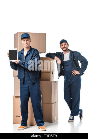 two movers with cardboard boxes looking at camera and presenting digital tablet with blank screen on white Stock Photo