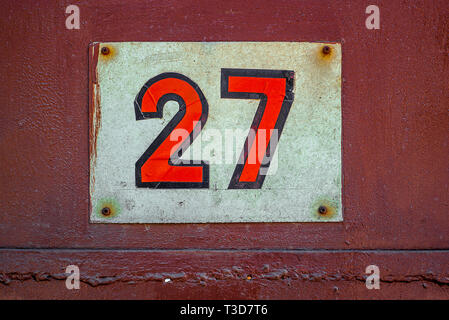 White Shabby Metal Plate With Red Nuber Twenty Seven Nailed On Red Old Metal Door Stock Photo
