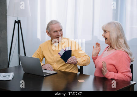 senior man holding air tickets and passports near surprised woman gesturing with hands at home Stock Photo