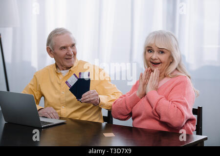 senior man holding air tickets and passports near surprised woman at home Stock Photo