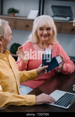 senior man holding air tickets and passports near surprised woman gesturing with hands at home Stock Photo