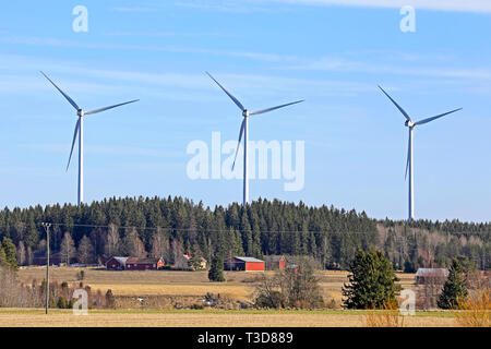 Row of three wind turbines near country village in South of Finland on a sunny day of spring. Stock Photo