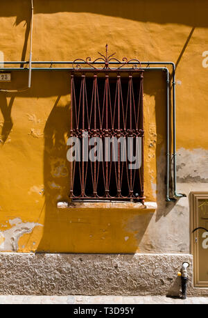 Detail of a rusted, ornate window grate and yellow plaster wall on the streets of Fano, Italy Stock Photo