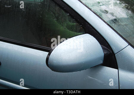 Raindrops on a side view mirror and windows of metallic blue car after rain close-up. Stock Photo