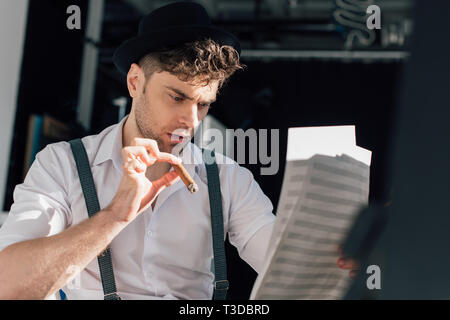 selective focus of handsome musician with cigar, reading notes on music book sheets Stock Photo