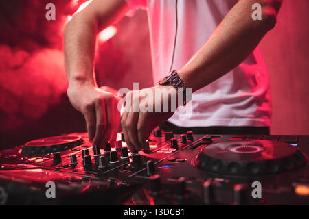 Dj mixing at party festival with red light and smoke in background - Summer nightlife view of disco club inside. Focus on hands Stock Photo