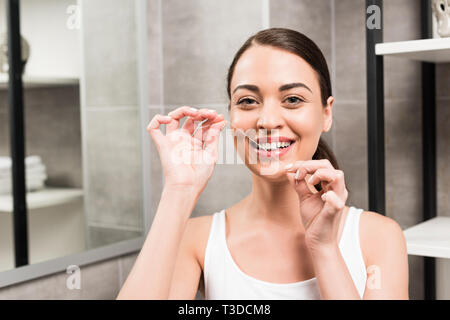 happy brunette woman using dental floss in bathroom Stock Photo