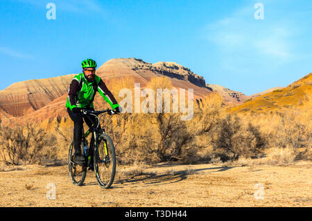 Young man on a bicycle. A trip through the desert territory. Cyclist in the desert. Cretaceous mountains Stock Photo