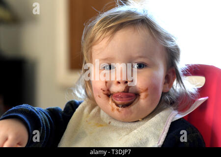 Baby girl feeding herself with chocolate on her face Stock Photo