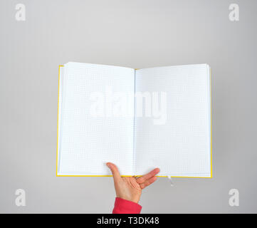 female hand holds open yellow notepad into a cell on gray background, copy space Stock Photo