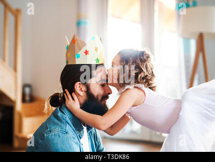 A side view of small girl with a princess crown and young father at home, playing. Stock Photo