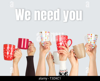 many hands raised up and holding ceramic cups on a gray background,  inscription we need you,  concept of recruitment in the company Stock Photo
