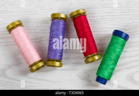 Four thread spools of different colours on a white wooden background Stock Photo