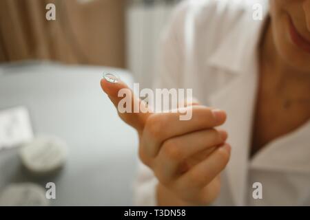 Female finger with contact lens on blurred background. Doctor in ophthalmology clinic. Stock Photo